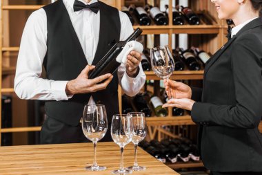 cropped shot of couple of wine stewards pouring wine into glass for degustation at wine store clipart