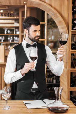 confident young sommelier examining color of wine at wine store clipart
