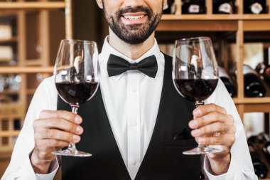 gülümseyen genç sommelier iki bardak kırmızı şarap şarap mağazasında holding in kırpılmış atış