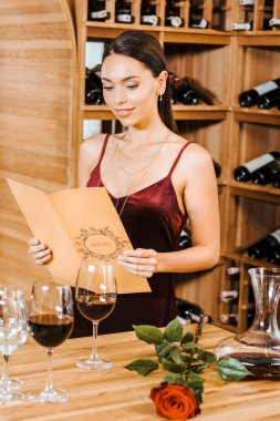 beautiful woman in red dress reading wine card at wine store clipart