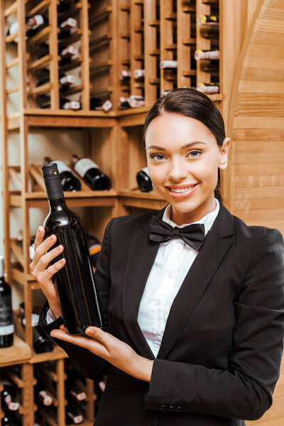 beautiful female wine steward holding bottle at wine store