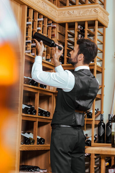 Красивый молодой сомелье положить бутылку на полку в винном магазине

