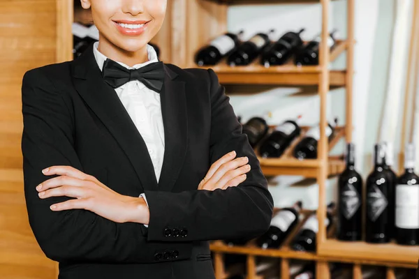 cropped shot of smiling female wine steward with crossed arms at wine store