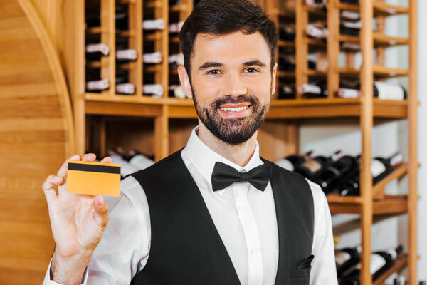 smiling young wine steward holding golden card at wine store