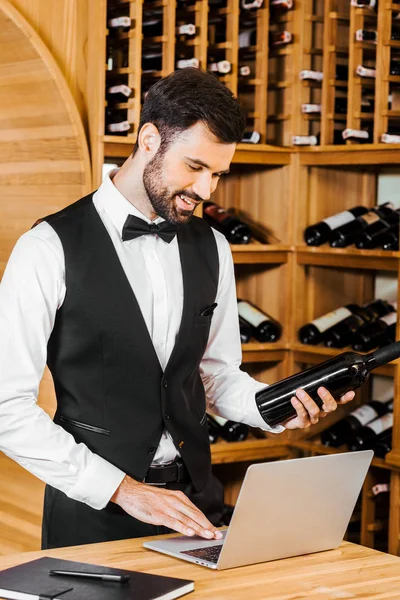 微笑的年轻品酒师与瓶葡萄酒在葡萄酒商店做笔记 — 免费的图库照片