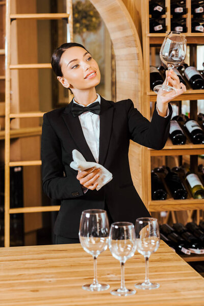 attractive female wine steward checking clear glass at wine store