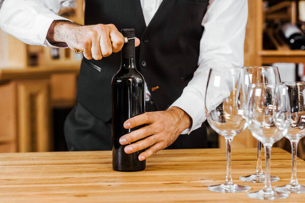 cropped shot of sommelier opening bottle of wine at store