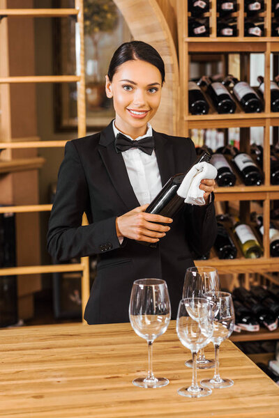 smiling female wine steward holding bottle at wine store