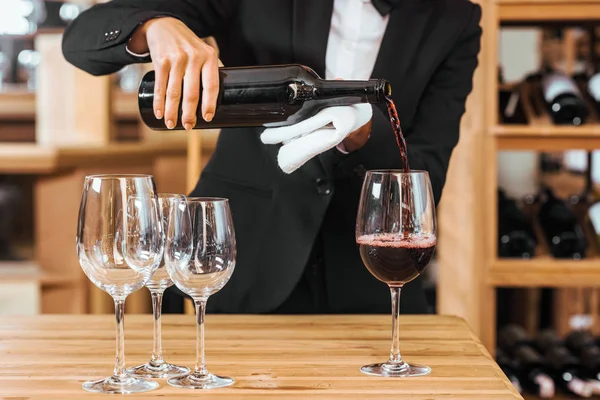 cropped shot of female wine steward pouring wine into glasses at wine store