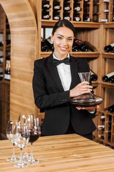 smiling female wine steward holding decanter at wine store