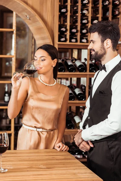 wine steward standing near woman while she tasting wine at wine store