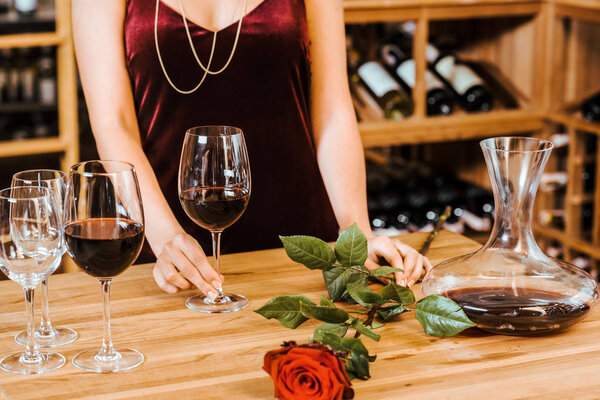 cropped shot of woman in red dress with wine glasses and rose at wine store
