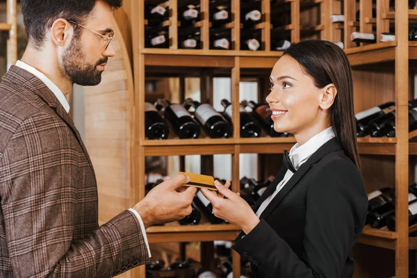 female wine steward taking credit card from customer at wine store