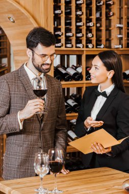 female wine steward showing menu list to client at wine store clipart
