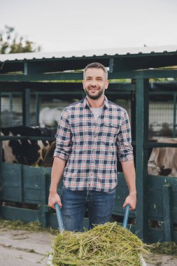 El arabası ile çim holding ve cowshed çalışırken kameraya gülümseyen çiftçi