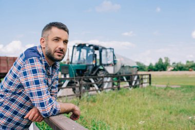 pensive middle aged farmer leaning at railing and looking away at farm  clipart