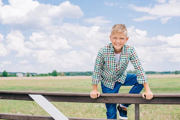 フェンスに登って ファーム上のカメラで笑顔の幸せな少年  — 無料ストックフォト