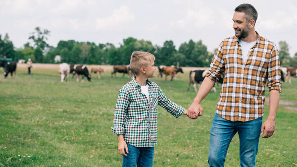 happy father and son holding hands and smiling each other at farm