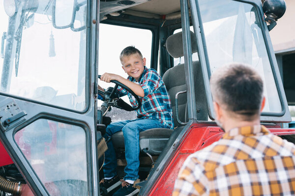 selective focus of father looking at happy son sitting in tractor