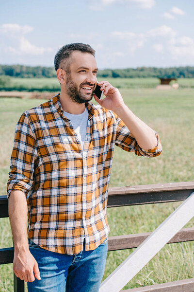 happy middle aged farmer talking by smartphone outdoors