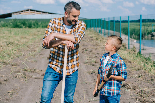 father and son holding shovels and looking at each other on farm