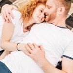 Vista de ángulo alto de feliz pareja joven tomados de la mano y acostados juntos en cuadros en el picnic