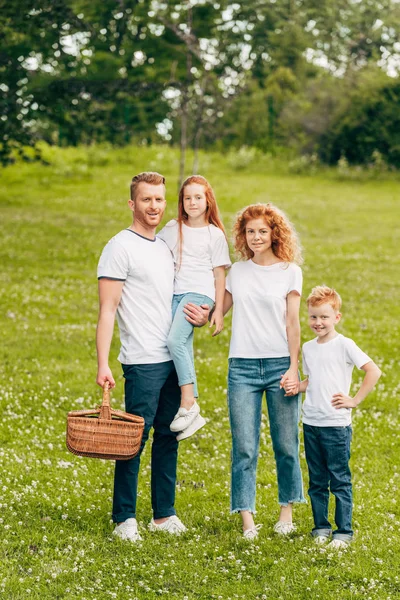 Glückliche Familie Lächelt Die Kamera Während Sie Mit Picknickkorb Park — kostenloses Stockfoto