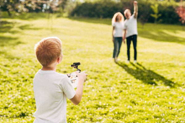 boy playing with drone while parents standing behind at park