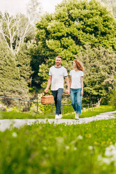 happy young couple with picnic basket walking in beautiful park