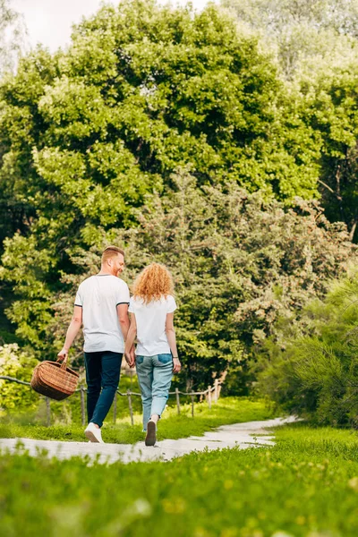 年轻夫妇与野餐篮步行在美丽的公园的背面视图 — 图库照片