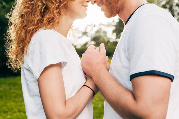 обрезанный снимок влюбленной молодой пары, держащейся за руки в парке
