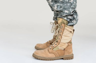 partial view of male soldier in camouflage clothing and boots on grey background clipart