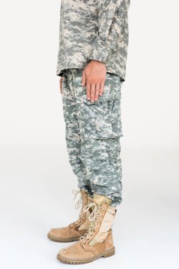 partial view of male soldier in camouflage clothing and boots on grey background clipart