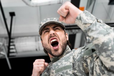 low angle view of emotional soldier in military uniform with blurred backdrop clipart
