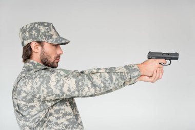 side view of male soldier in military uniform holding gun isolated on grey clipart