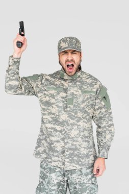 screaming male soldier in military uniform holding gun isolated on grey clipart