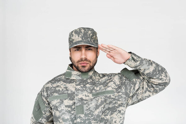 портрет уверенного бородатого солдата в военной форме, салютующего изолированно на сером
