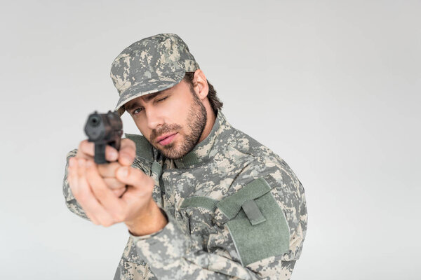 selective focus of male soldier in military uniform holding gun isolated on grey