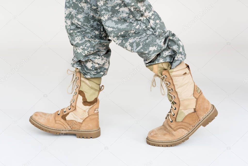 partial view of male soldier in camouflage clothing and boots on grey background