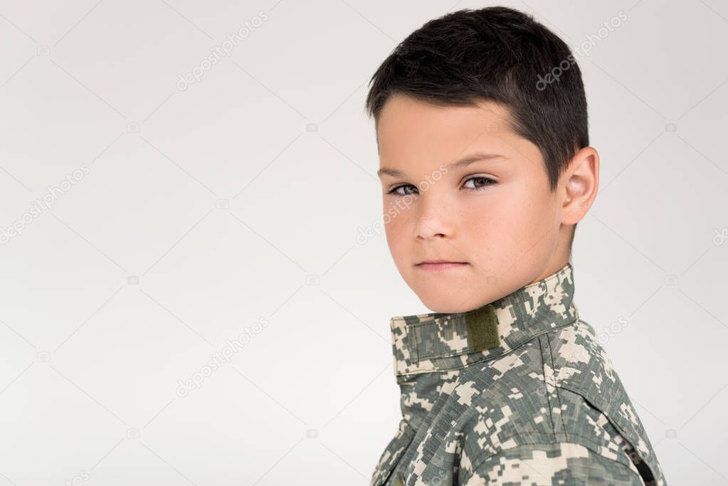 side view of kid in military uniform looking at camera on grey background