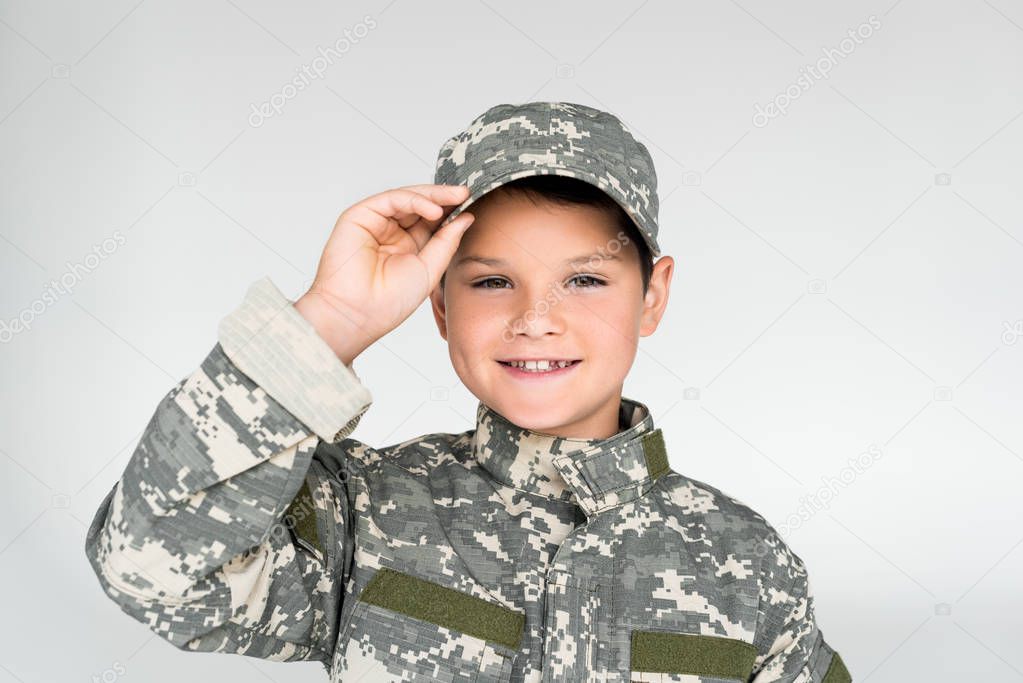 portrait of smiling kid in military uniform posing on grey background