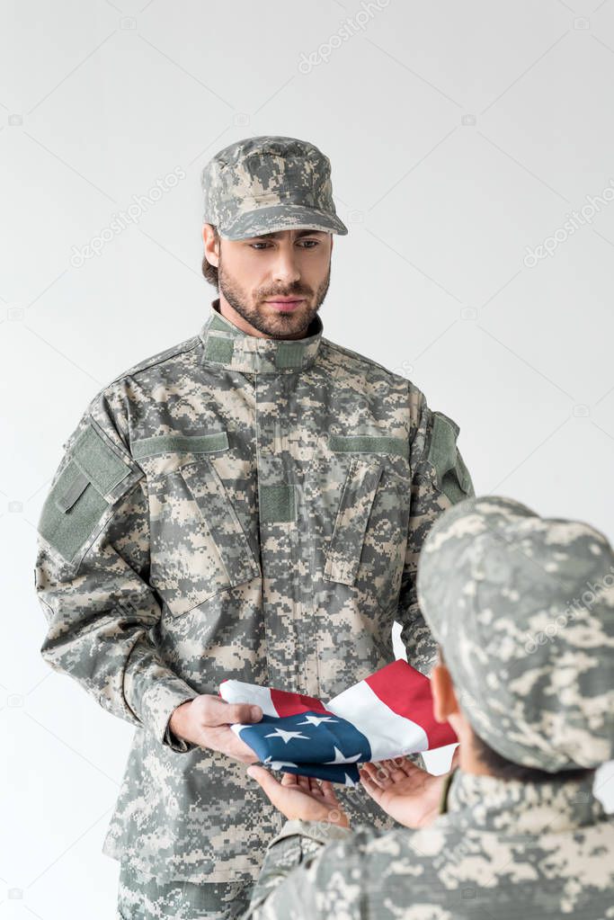 partial view of soldier giving folded american flag to kid in camouflage clothing on grey background