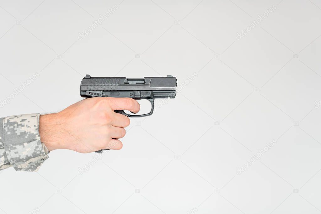 cropped shot of male soldier holding gun on grey backdrop