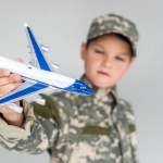 Selective focus of little boy in military uniform with toy plane in hand isolated on grey