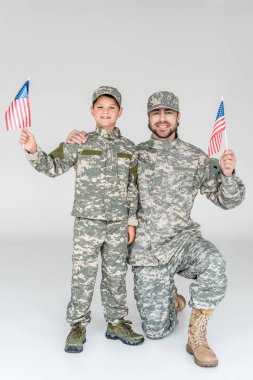 Baba ve oğul Kamuflaj giyim gri arka plan üzerinde elinde Amerikan bayrak direkleri ile gülümseyen