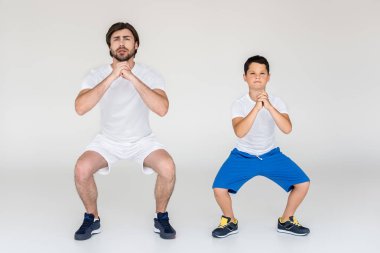 boy and father squatting together on grey background clipart
