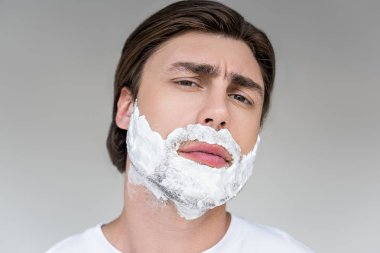 portrait of handsome man with shaving foam on face looking at camera isolated on grey clipart