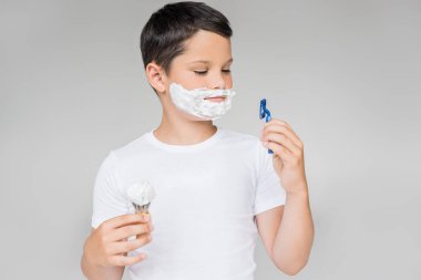 portrait of preteen boy with razor, brush shaving foam on face isolated on grey clipart