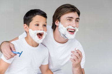 excited father and son with shaving foam on faces isolated on grey clipart
