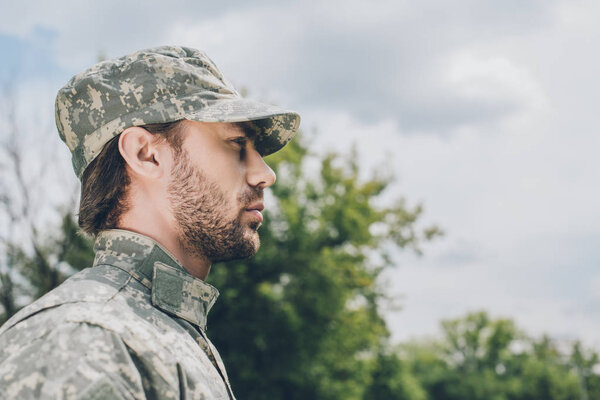 вид сбоку уверенного солдата в военной форме на фоне облачного неба
